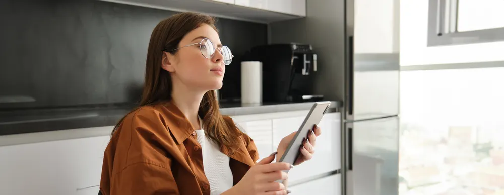 Frau mit Brille sitzt in der Küche und schaut auf ein Tablet