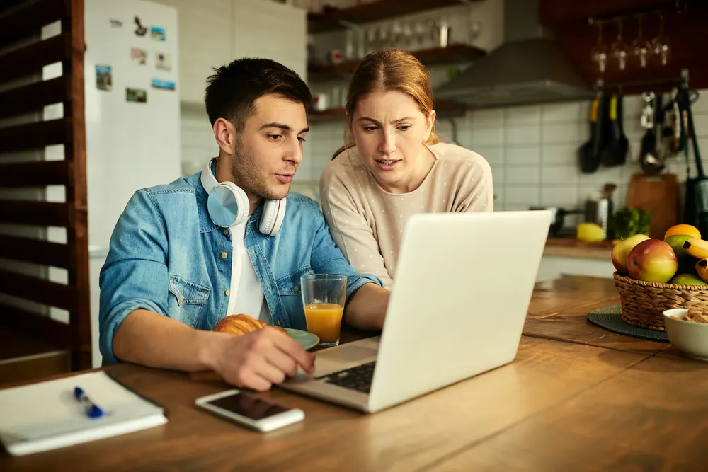 Paar sitzt mit Laptop am Küchentisch und vergleicht Angebote